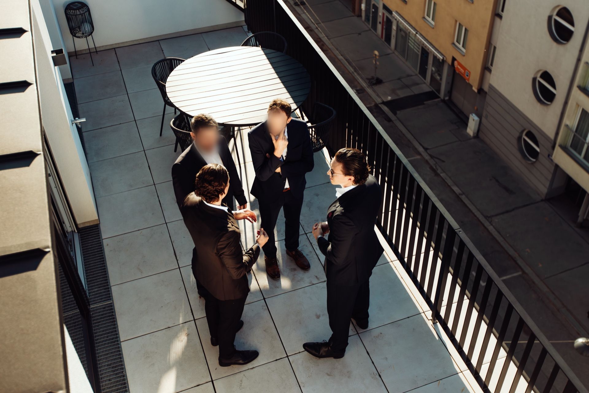 Four men in dark suits in conversation on a sunny terrace, photographed from above
