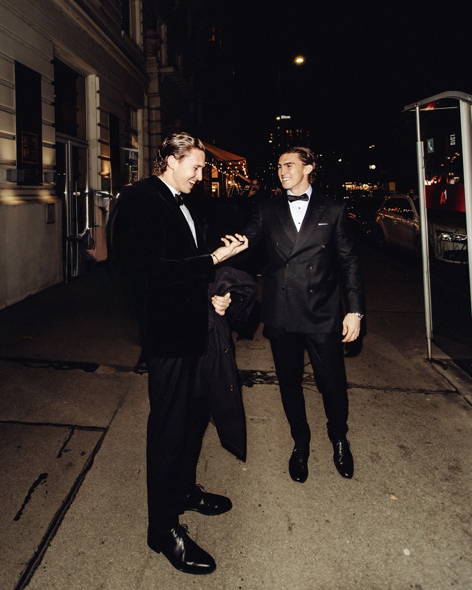 Two gentlemen in dinner jackets laughing together at night on a lit street in Vienna, one carrying his coat over his arm