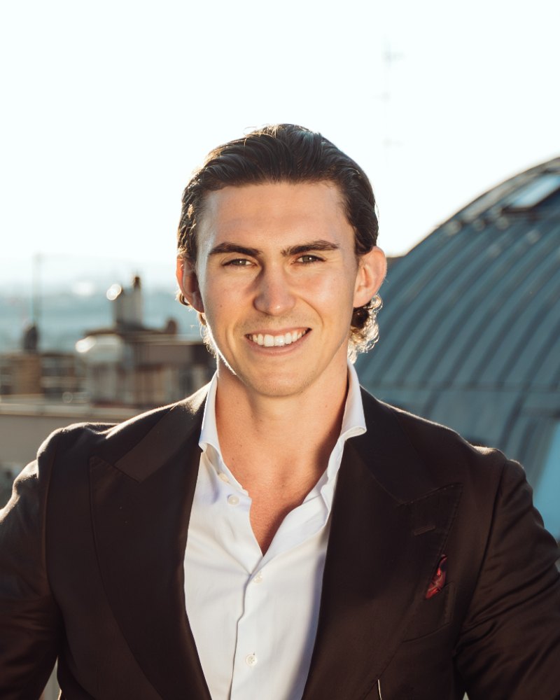 Portrait of Matthias Nussbaumer smiling in a dark suit and white shirt on a rooftop terrace above Vienna