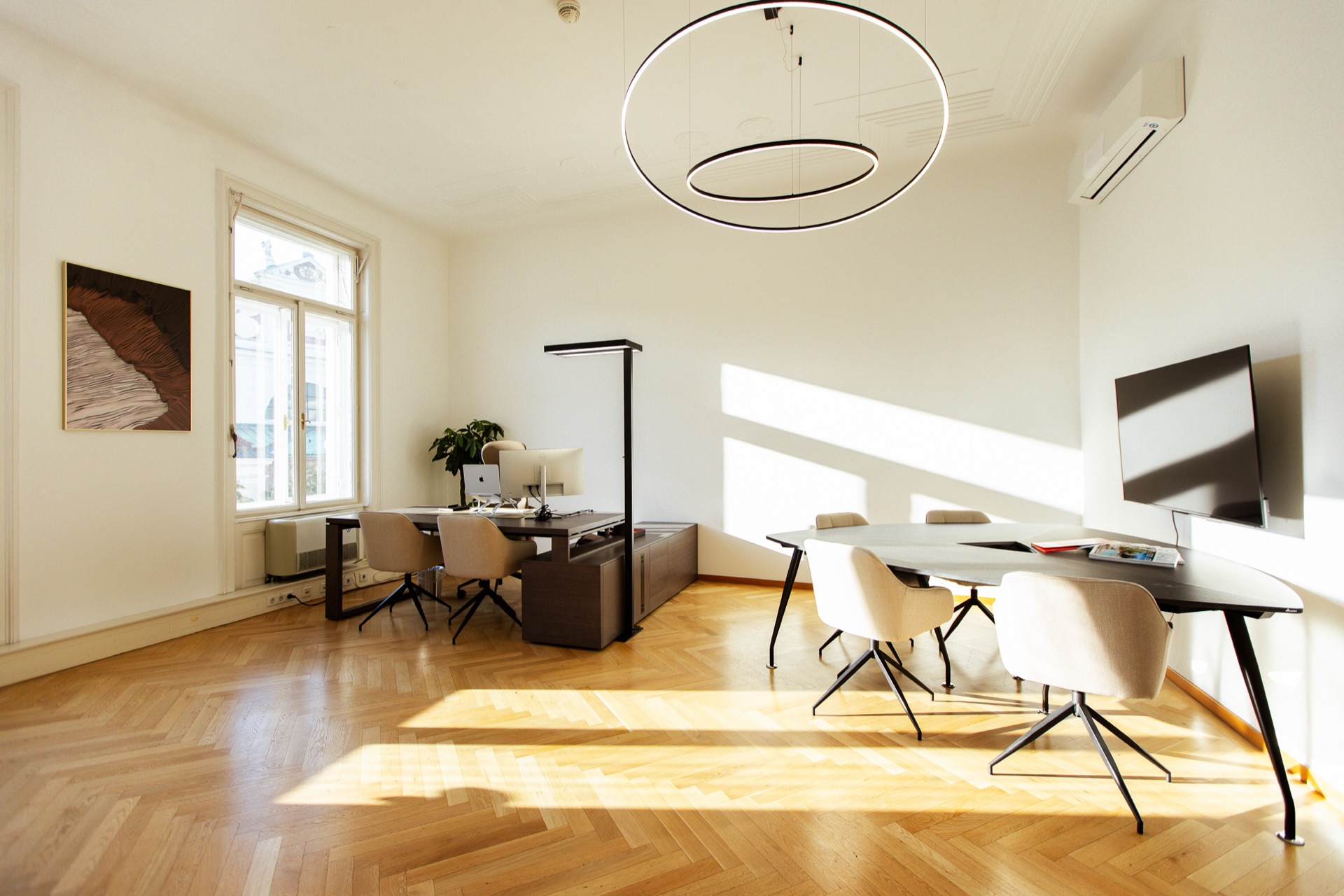 Sunlit office in a Viennese period building with herringbone parquet, a round pendant lamp and a meeting table