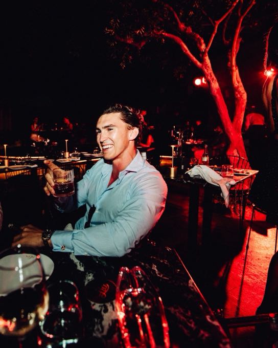 Host with a glass at an evening table beneath a tree lit in red