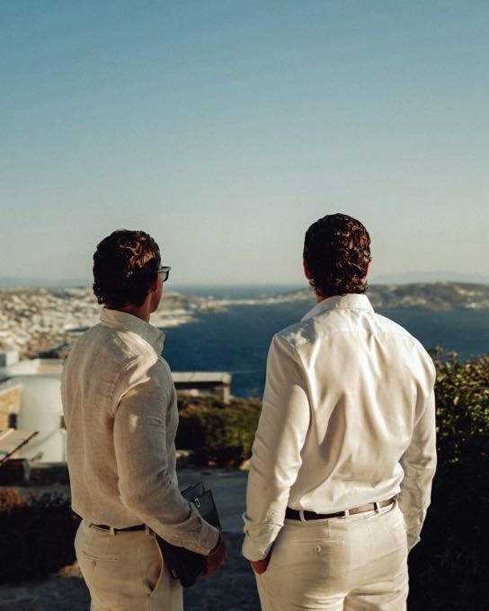 Two men in light shirts looking out over the sea from a hilltop