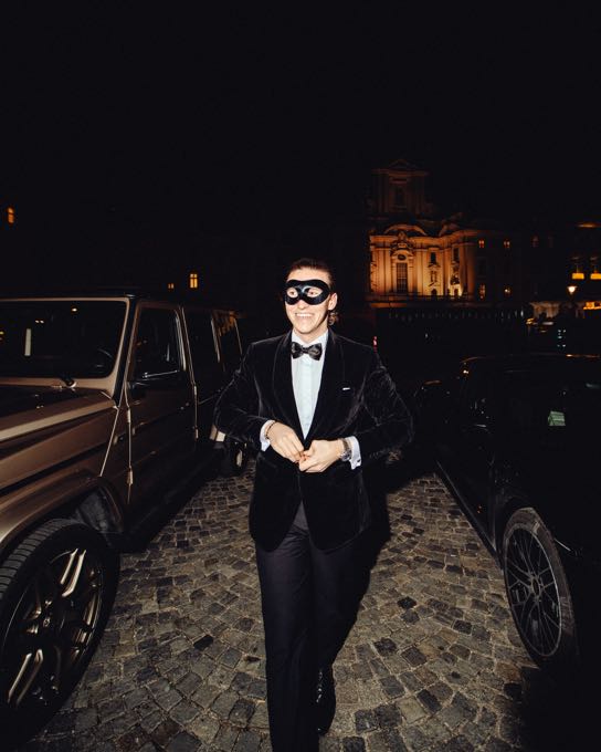Man in a dinner jacket and eye mask in front of a car at night
