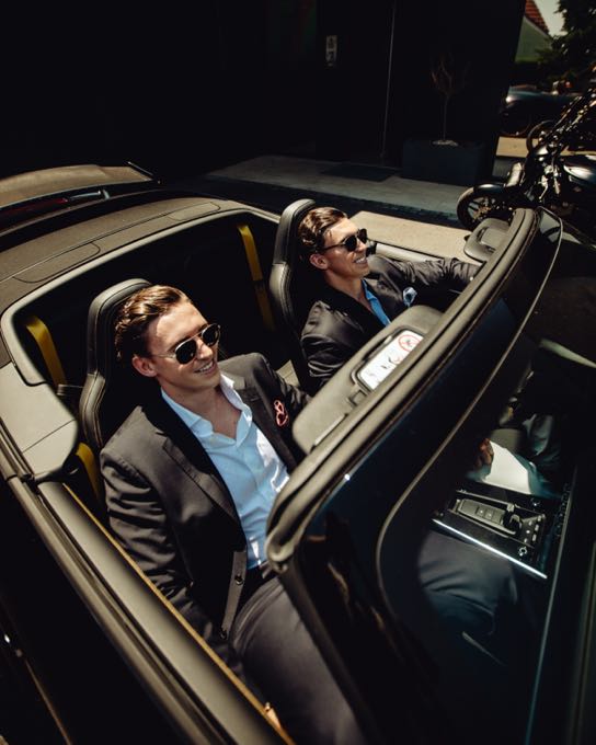 Two men in sunglasses in an open sports car at night