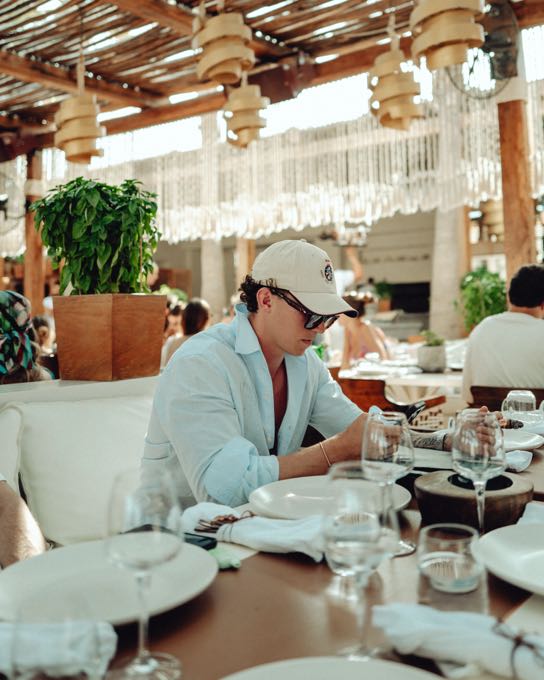 Man in a cap dining on a terrace with rattan lamps