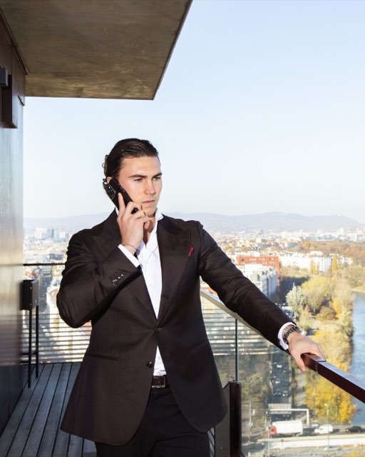Man in a dark suit on the phone on a balcony high above the city