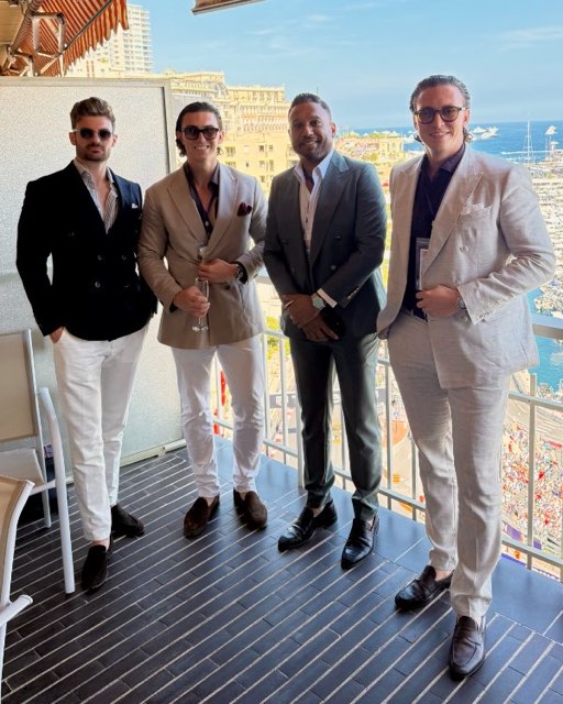 Four men in suits on a balcony with a red and white striped awning above the harbour