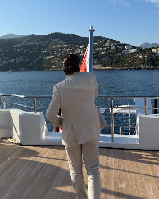 Man in a light suit on the deck of a yacht looking towards the coast