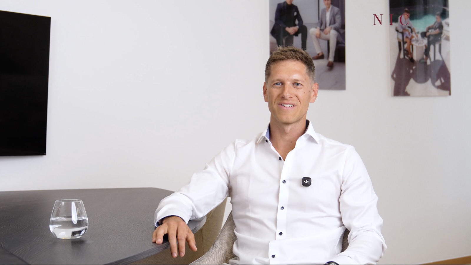 Samuel H. im weißen Hemd sitzt lächelnd im NIC Büro an einem dunklen Tisch